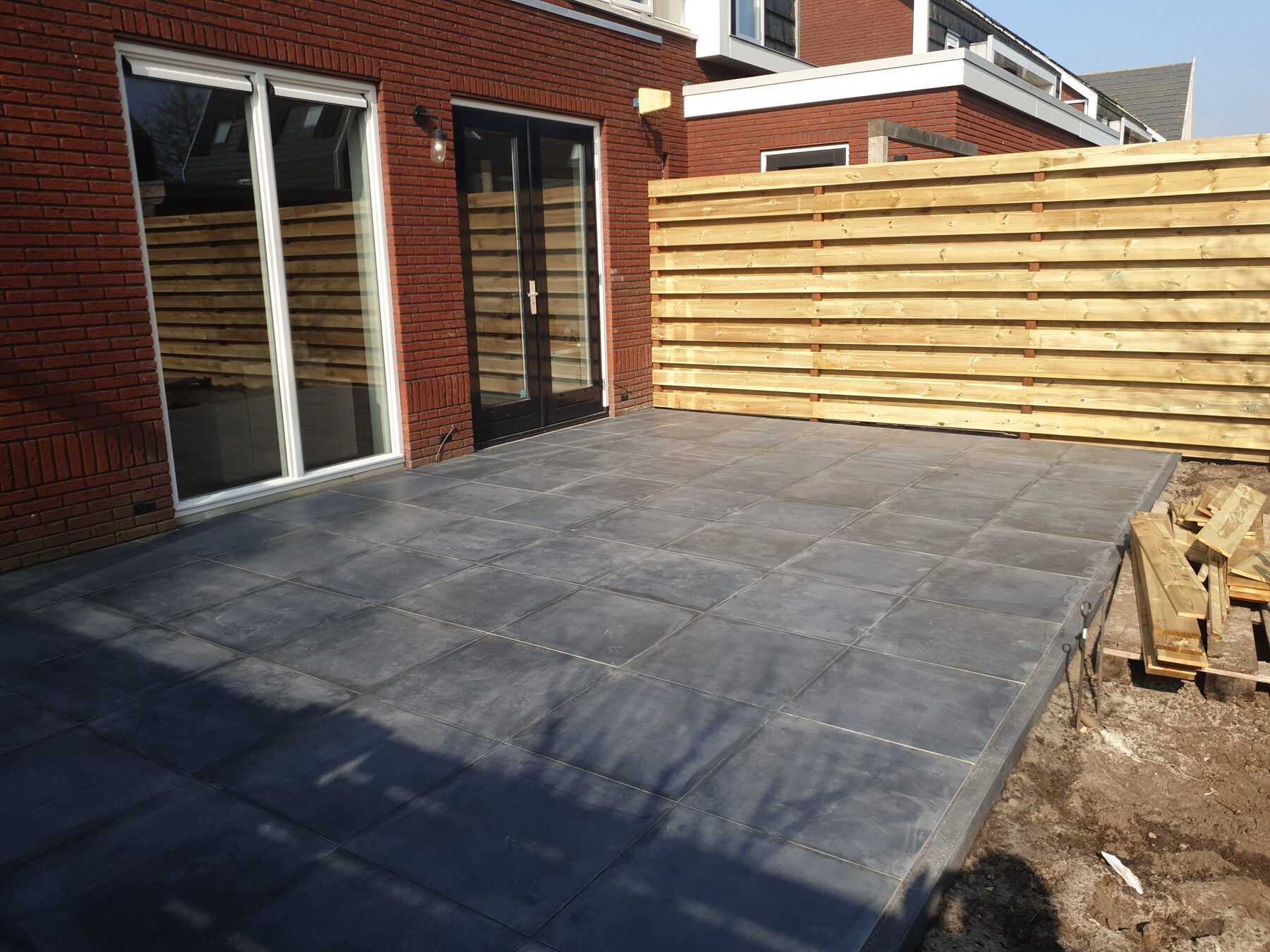 Nieuw aangelegd bestraat terras met houten erfafscheiding
